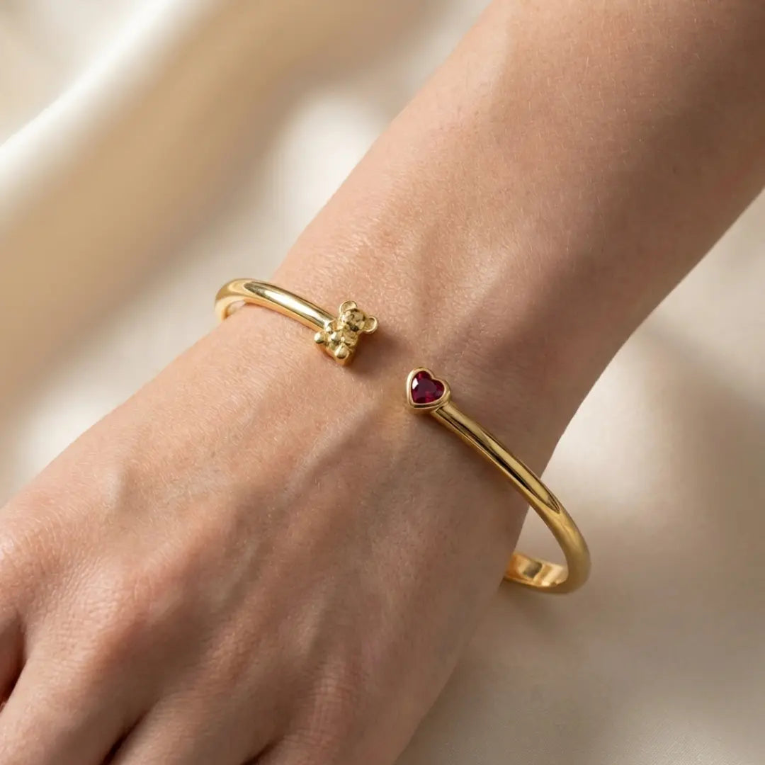 Gold Koala bangles with heart-shaped ruby on a wrist against a neutral background