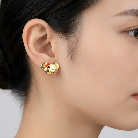 Gold Koala earrings with a red enamel bow worn by a person on a light grey background