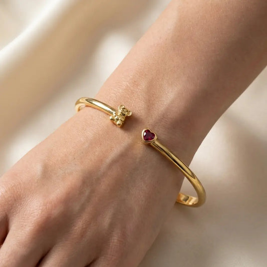 Gold Koala bangles with heart-shaped ruby on a wrist against a neutral background