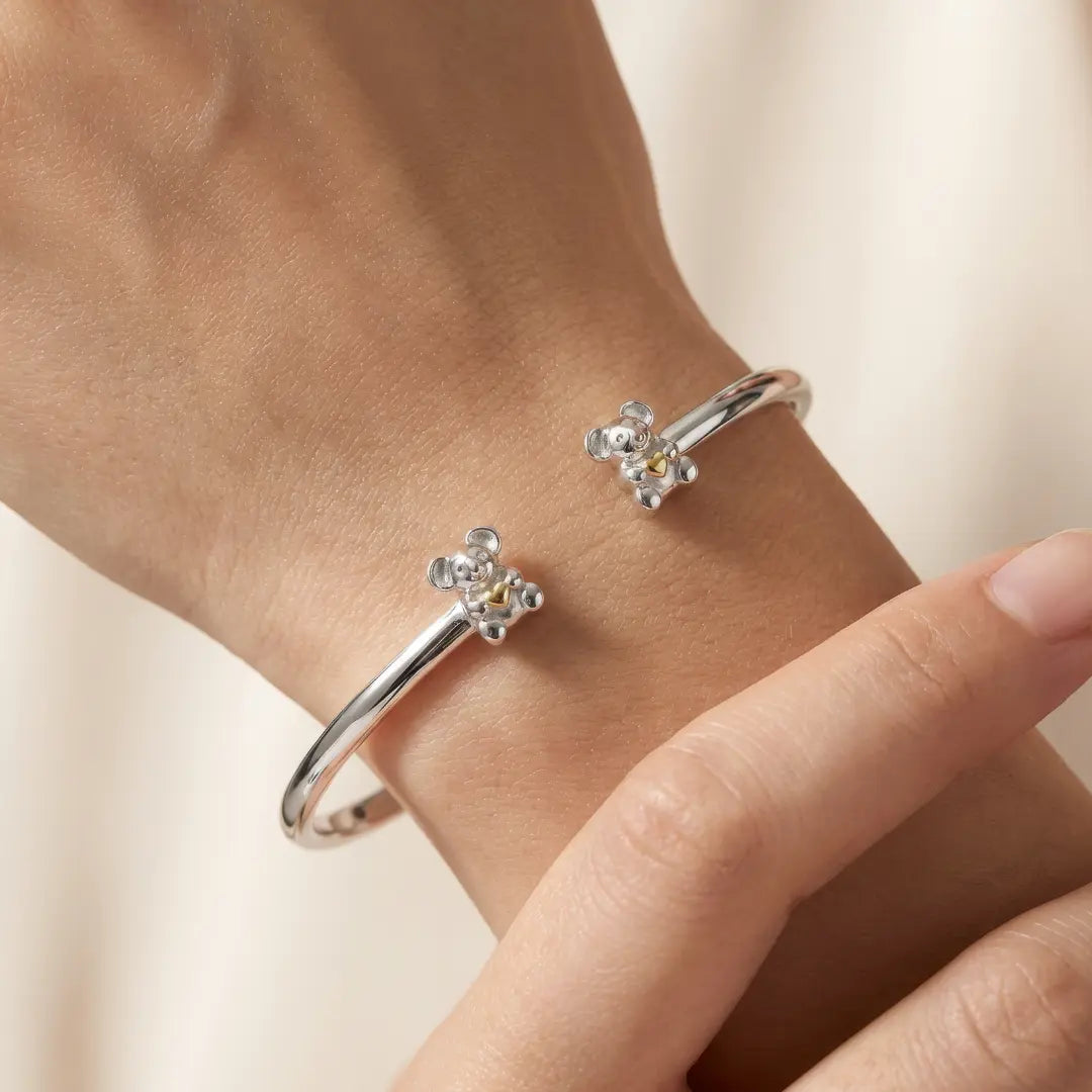 Silver bangle with Koala designs on a wrist against a neutral background