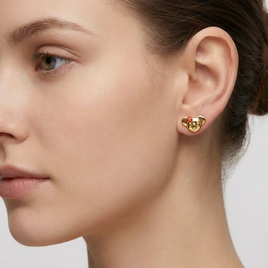 Close-up of a woman wearing gold Koala shaped earrings with red enamel flower on a neutral background